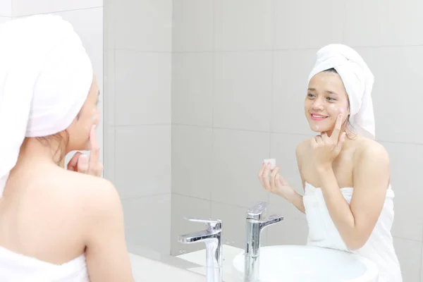 浴室で入浴後の彼女の顔にクリームを適用する幸せな女の画像 — ストック写真