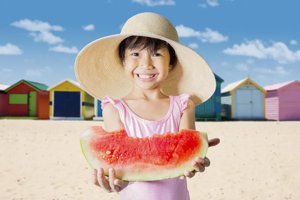 夏天的概念 小女孩拿着一块新鲜的西瓜 而微笑着在相机和站在沙滩上 — 图库照片