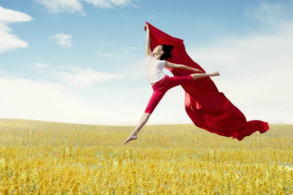 アジアの女性バレリーナ持株赤いファブリックの草原に大きなジャンプを作るします 夏や春のコンセプト — ストック写真