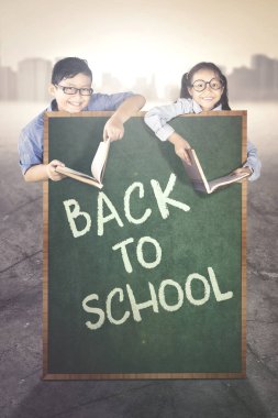 İki küçük öğrenciler okula geri süre kitaplarla eğitim kara tahta üzerinde bir metnin arkasına