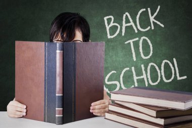 Bir kitap okuma ve okula geri tahtada metinle oturan bir bilinmeyen liseli kız resmi