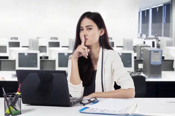 年轻的女商人在办公室里用笔记本电脑示意她的食指在嘴唇上保持沉默 — 图库照片