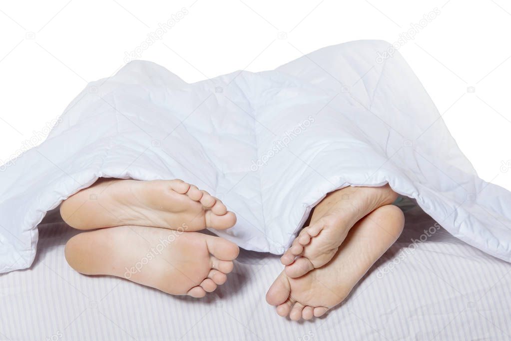 Feet of young couple sticking out from under a blanket during sleeping together on the bed, isolated on white background