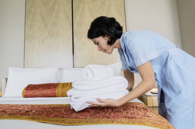 Kadın hizmetçi temiz havlu yığını çarşaf üzerinde koyarak görüntüsü. Otelin vurdu