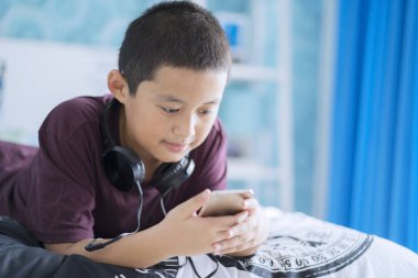 Yatakta yatıyordu süre bir smartphone kullanarak küçük şirin bir çocuk resmi. Evde vurdu