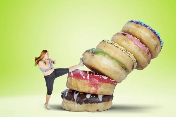 ドーナツの山を蹴ることによって甘い食べ物を食べることを拒否太った女性の画像 グリーン スクリーンの背景で撮影します — ストック写真
