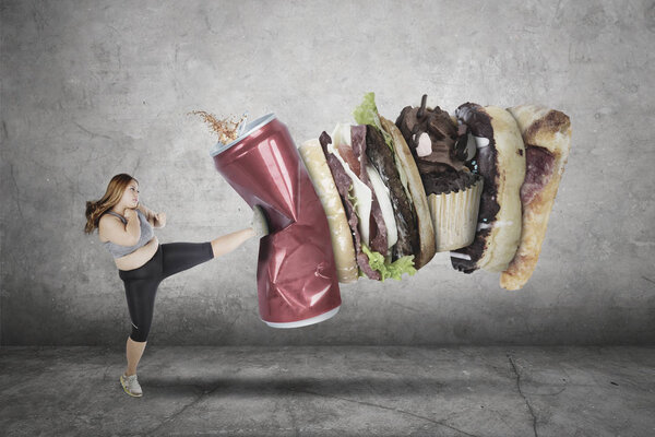 Portrait of fat woman wearing sportswear while kicking unhealthy food and drink with green screen background
