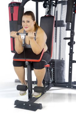 Beyaz arka plan üzerinde izole bir ağırlık makine ile egzersiz yaparken kameraya gülümseyen güzel şişman bir kadın portresi