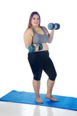 Beyaz arka plan üzerinde izole iki dumbbells ile bir egzersiz yaparken kameraya gülümseyen güzel şişman kadın portresi