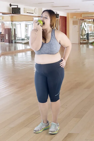 フィットネス センターで新鮮なリンゴを食べながらスポーツウェアを着て美しい太った女性の完全な長さ — ストック写真