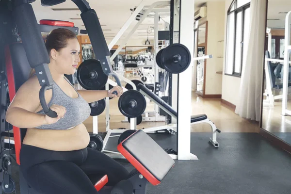 Image of Caucasian fat woman exercising with press machine. Shot in the gym center