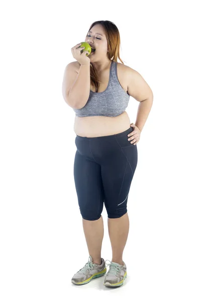 青リンゴ 白い背景で隔離を食べながらスポーツウェアを着ている肥満の女性の完全な長さ — ストック写真