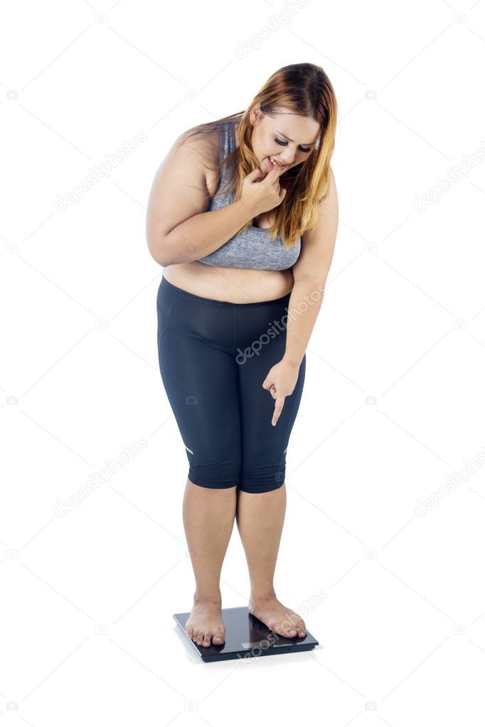 Portrait of overweight woman looks scared while standing on the weighing scale, isolated on white background