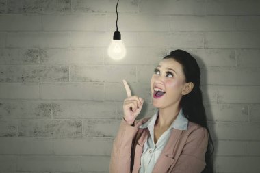 Bir beyaz kadın girişimci parlak bir ampul bakarken bir fikre kapılmasını resmini