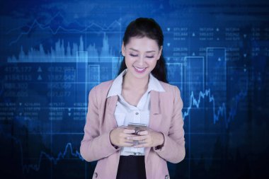 Beyaz kadın girişimci bir cep telefonu kullanarak ve büyüme ekonomi grafik arka planı ile ayakta iken mutlu görünüyor