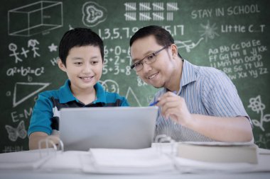 Görüntü Asyalı öğretmen öğrencisini sınıfta otururken bir dizüstü bilgisayar kullanmak kılavuzları