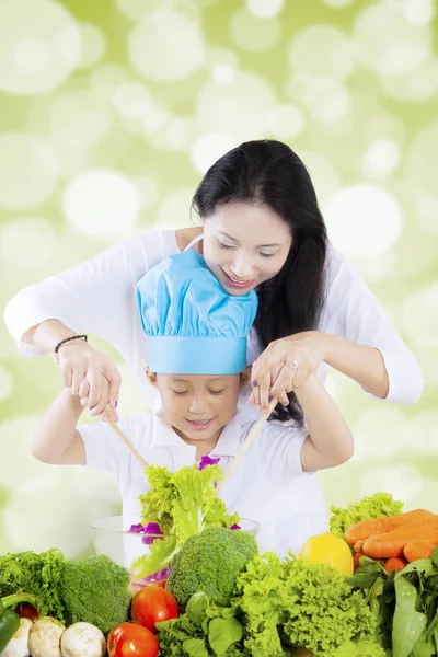 Sevimli küçük çocuk ve annesi ile birlikte tablo sebze, dolu salata bir kase bokeh arka plan ile vurdu