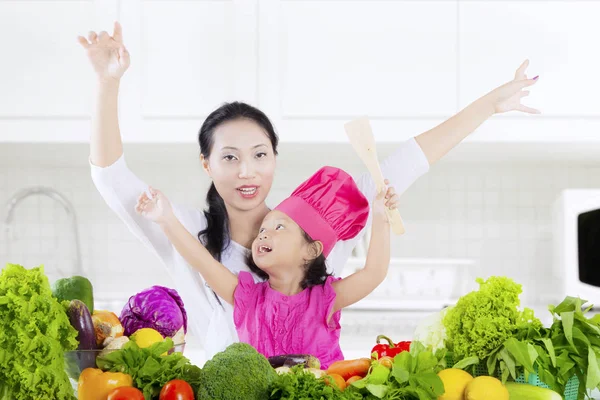 小さな女の子と彼女の母親は テーブルの上の新鮮な野菜とキッチンで手を上げる自宅撮影 — ストック写真