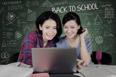 Bir dizüstü bilgisayar birlikte sınıfta kullanılması ve ile oturan iki kadın üniversite öğrencilerinin resim tahta doodles