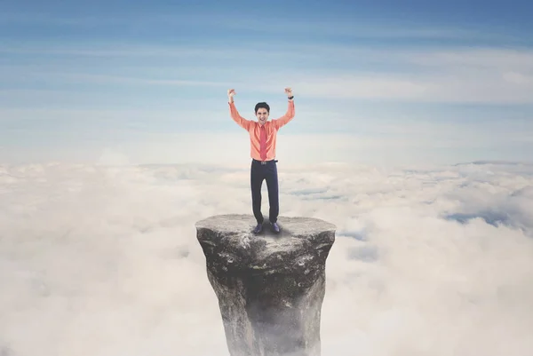 男性の起業家の手を持ち上げる山の頂上に立っている間彼の成功を祝うために — ストック写真