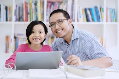 Asyalı erkek öğretmen öğrencisini kütüphanede ile bir dizüstü bilgisayar kullanırken kameraya gülümseyen portresi