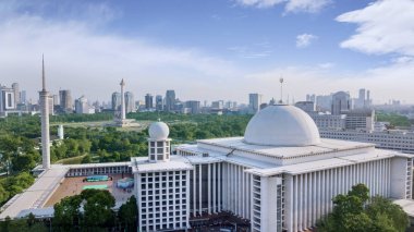 Jakarta - Endonezya. 24 Temmuz 2018: İstiklâl Camii ile ulusal anıt ve gökdelenler içinde belgili tanımlık geçmiş mavi gökyüzü altında