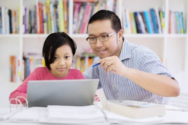 Genç adam portresi kütüphanede otururken bir dizüstü bilgisayar kullanmak için küçük bir kız öğretir