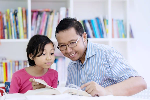 年轻教师的图片指导他的小学生读一本书 而坐在图书馆 — 图库照片