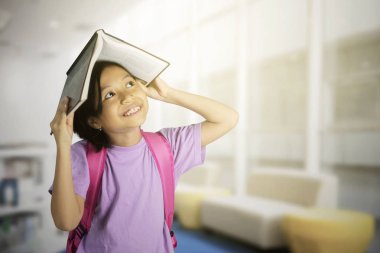 Şirin kız öğrenci resmini açık bir kitap kafasında kütüphanede bir şeyler düşünmeye süre koyar