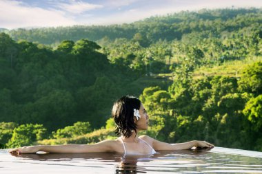 Asyalı kadın güzel dağ manzarası tadını çıkarırken yüzme havuzunda rahatlatıcı resim