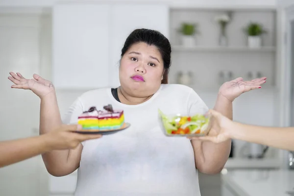 困惑超重的女人不知道什么选择彩虹蛋糕和沙拉 — 图库照片