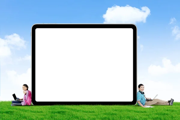 人の小学生の写真は ラップトップで勉強と草原の空白のホワイト ボードの近くに座って幸せそうに見える — ストック写真