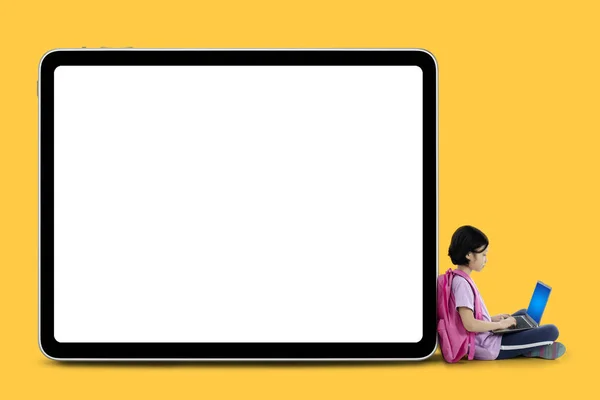 在空白白板旁边坐着一台笔记本电脑的聪明女生图片 黄色背景拍摄 — 图库照片