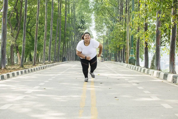 道を全力疾走しながらカメラに向かって笑みを浮かべて太った女性のイメージ — ストック写真