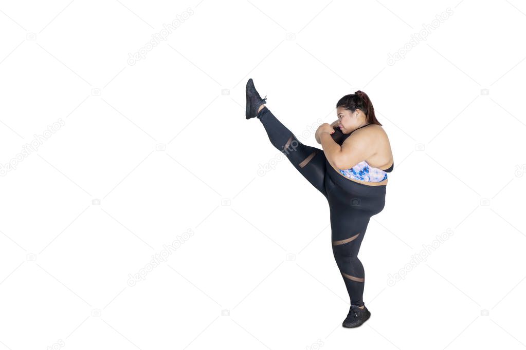 Portrait of Asian obese woman wearing sportswear while practicing a high kick, isolated on white background