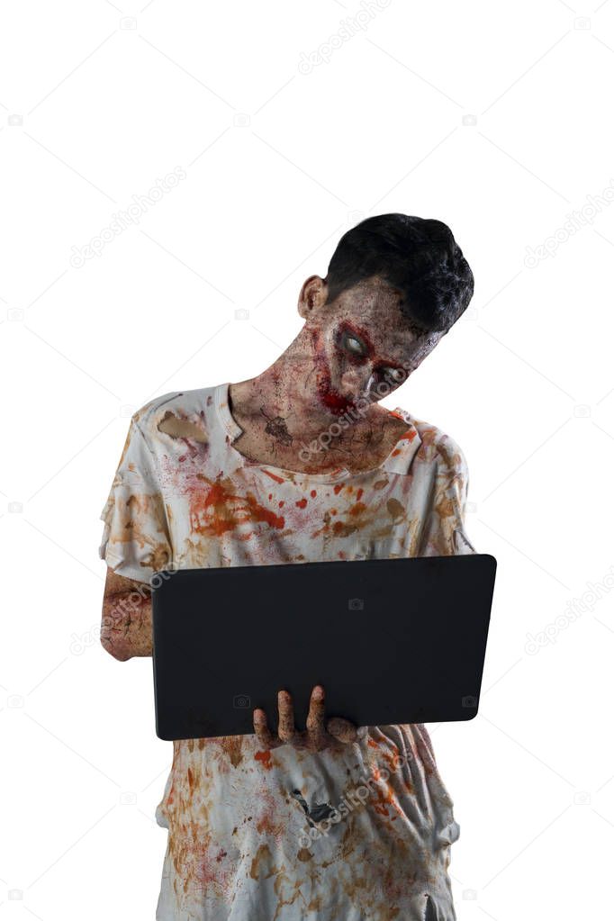 Halloween horror concept. Image of creepy male zombie holding a laptop and standing in the studio