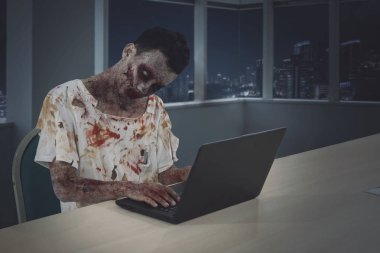 Resmi erkek zombi ofiste otururken dizüstü bilgisayarla çalışma. Gece zaman vurdu