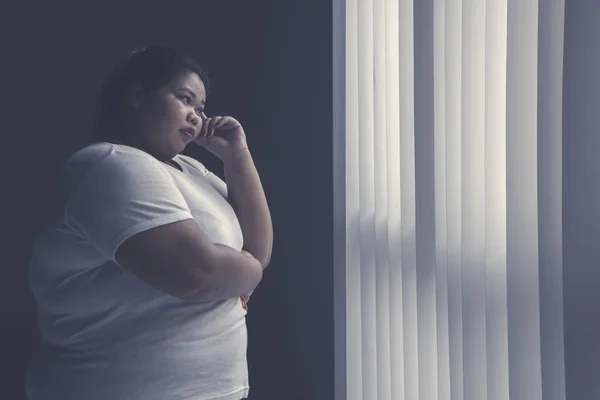 照片的胖女人在思考的东西 而站在窗口 — 图库照片