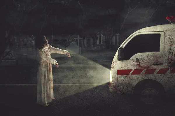 Halloween horror concept. Picture of scary zombie woman hindering an ambulance car in the grave. Shot at night time