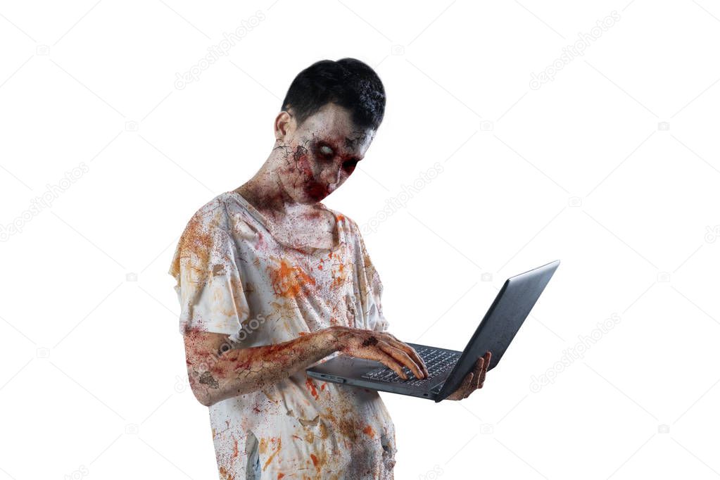 Halloween horror concept. Picture of horrible male ghost is looking at the camera while using a laptop in the studio