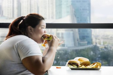 Pencerenin kenarında otururken restoranda hamburger yeme şişman kadın resim