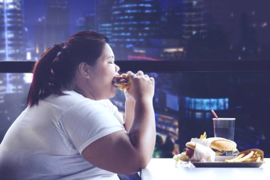 Şişman kadın restoranda yemek yerken bir hamburger ısırma yan görünüm