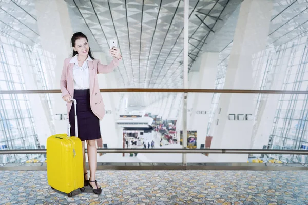 美丽的女商人站在一个手提箱 而采取自拍照片使用智能手机在机场候机楼 — 图库照片