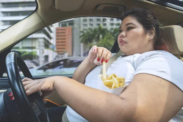 超重妇女在开车上路时吃薯条的形象 — 图库照片