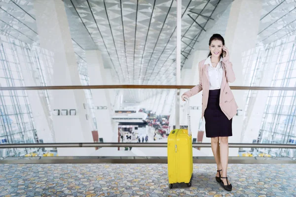 一个漂亮的企业家的图片与手机交谈时 站在一个手提箱在机场候机楼 — 图库照片