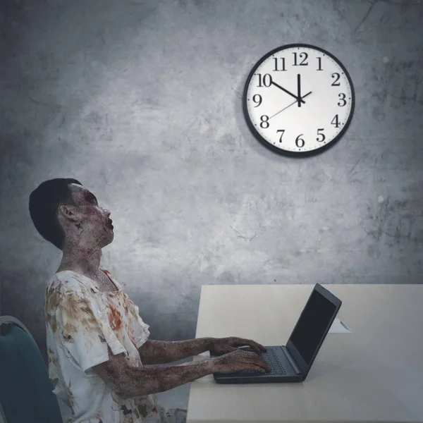 Obraz Przerażające Zombie Mężczyzna Patrząc Zegar Podczas Przepracowaniem Biurze — Zdjęcie stockowe