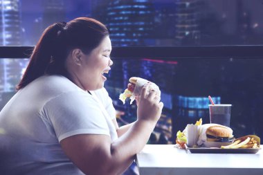 Picture of young obese woman having dinner with junk food in the restaurant clipart