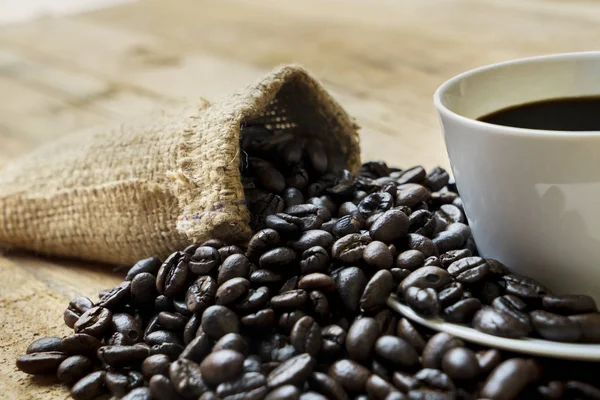用咖啡豆和麻布袋在木桌上关闭咖啡杯 — 图库照片