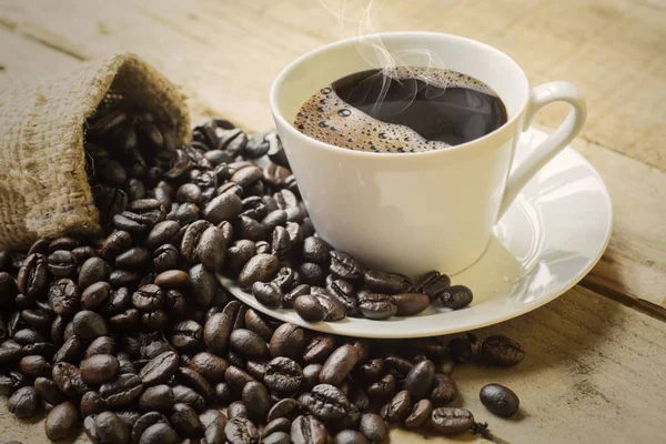 木桌上的咖啡豆和粗麻布袋的热黑咖啡杯 — 图库照片