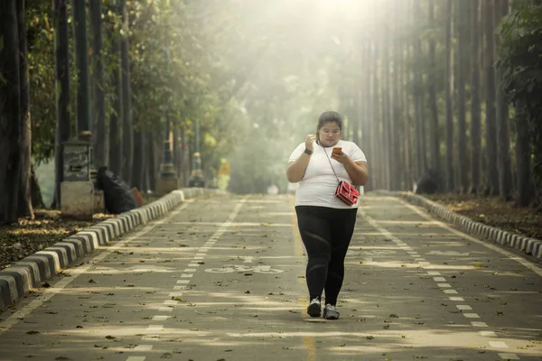Image of obese woman using a mobile phone while walking on the road
